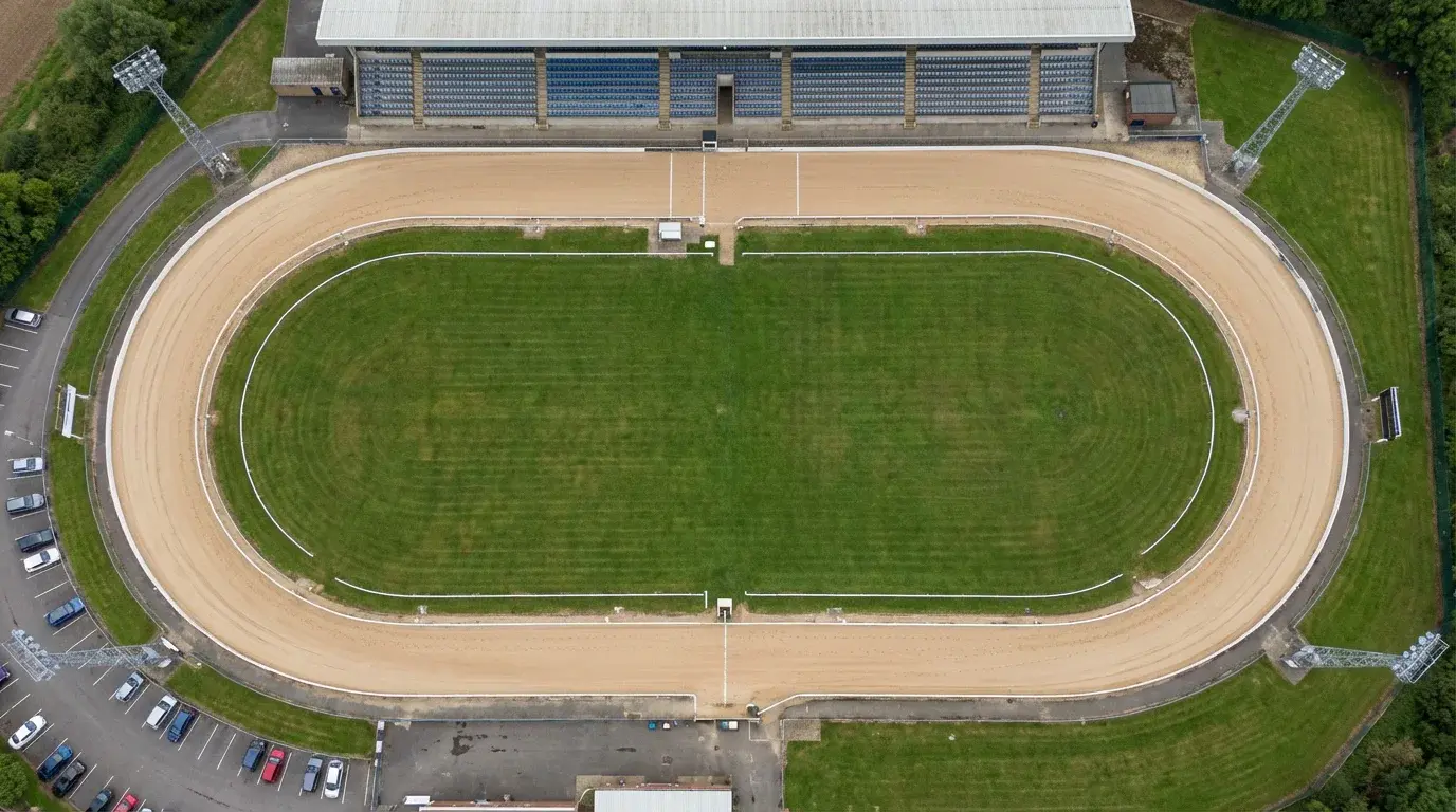 Aerial view of a UK greyhound racing stadium with the sand oval track and grandstand visible